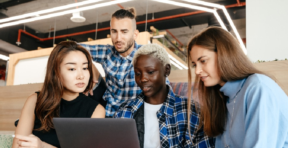 A diverse group of professionals working together, looking at a laptop screen.