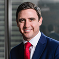 Man in a business suit with a red tie, smiling in an office setting.