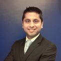 Person smiling in a suit against a blue background.