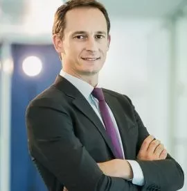 Businessman in a suit with arms crossed and a confident smile indoors.