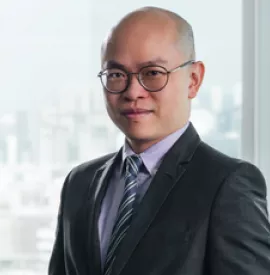 Man in a suit and tie standing in front of a window with a cityscape background.