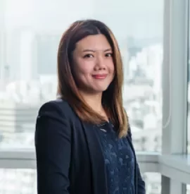 Woman in a suit smiling in an office with cityscape view.
