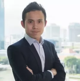 Person in a suit with arms crossed, standing in front of a cityscape.