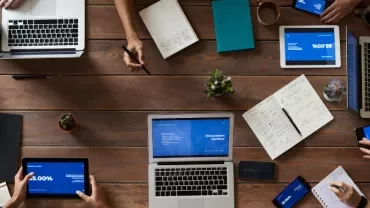 People working on laptops and tablets at a wooden table.