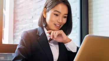 Businesswoman smiling while working on a laptop at her desk.
