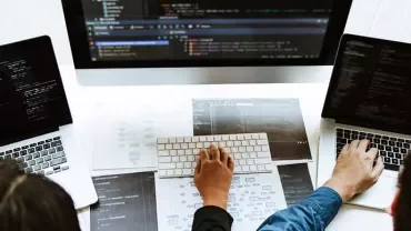 Three people working on laptops with code on screens.