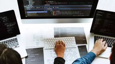 Three people working on laptops with code on screens.
