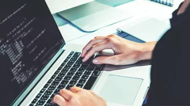 Person coding on a laptop with screen displaying lines of code.