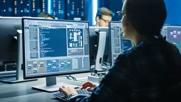 Person coding on computer in a dark room with screens