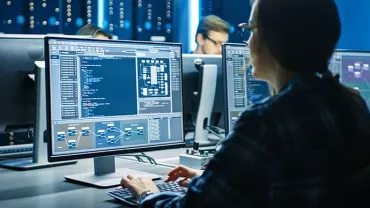Person coding on computer in a dark room with screens