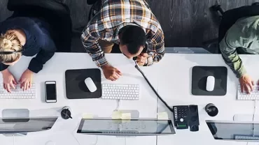 Three people working at computers in an office setting, viewed from above.