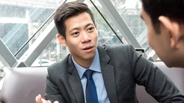 Two colleagues in suits having a discussion in a modern office setting.