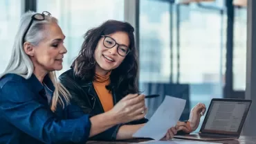 Two women of different age groups and ethnicities looking through a document together