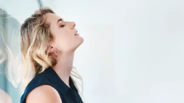 Woman with closed eyes leans against a glass surface, appearing relaxed.