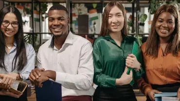 Four colleagues smiling and holding folders in an office setting.