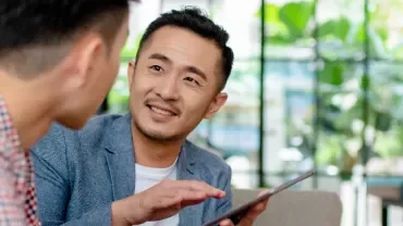 A male professional holding a tabelt and in discussion with another male professional