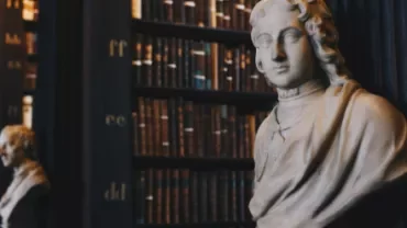 Marble bust in a historic library with bookshelves in the background.
