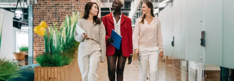 Three professionals walking in a modern office corridor with brick and glass walls.
