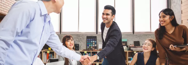 Group of professionals in a meeting, two men shaking hands.