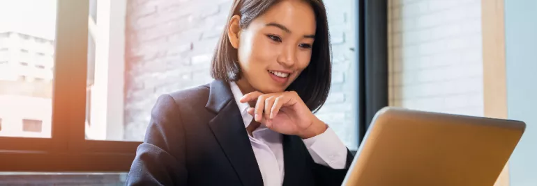 image of female Asian white collar employee worker sitting in front of a laptop smiling