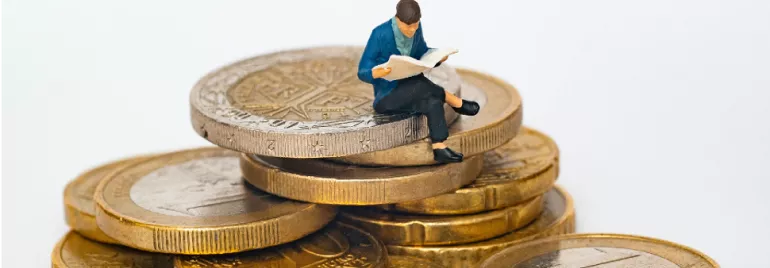 human figurine reading a book and sitting on a stack of coins