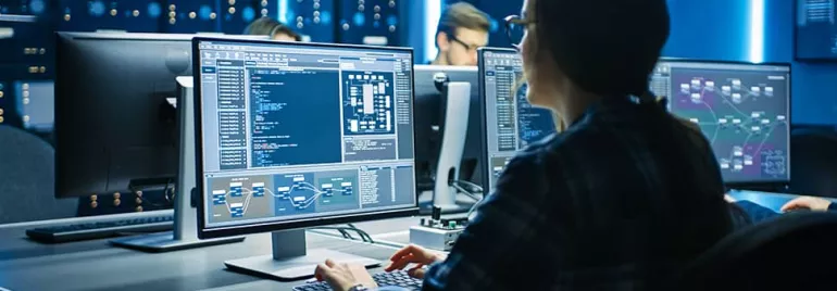 Person coding on computer in a dark room with screens