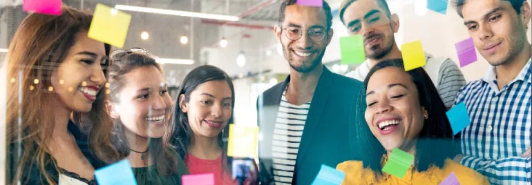 A diverse group of people brainstorming with colorful sticky notes on a glass wall.