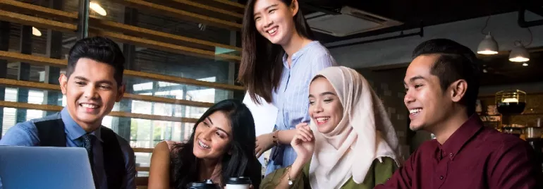 Group of five people smiling and looking at a laptop screen in an office setting.