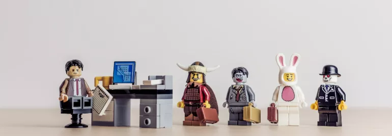 Lego figures dressed in various costumes standing in line at an office desk.