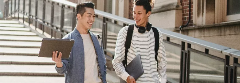 Two students walking down stairs, holding laptops and smiling.
