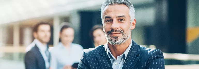 Confident man in a suit standing in front of a blurred group of professionals.