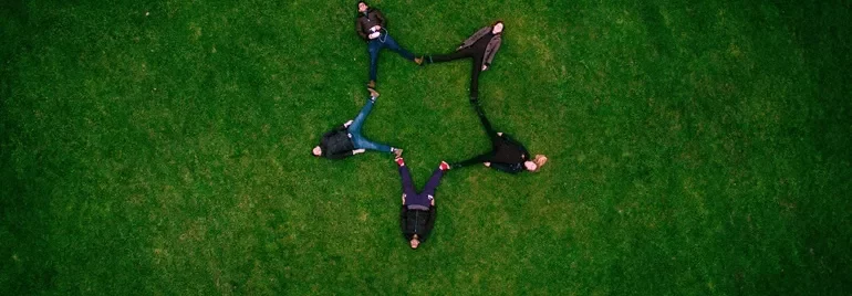 Five people laying on the grass forming a star shape
