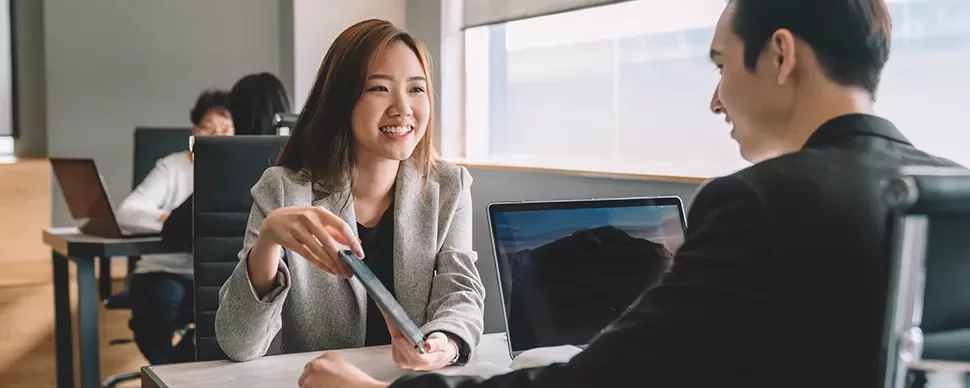 Two professionals talking at a table in an office setting.