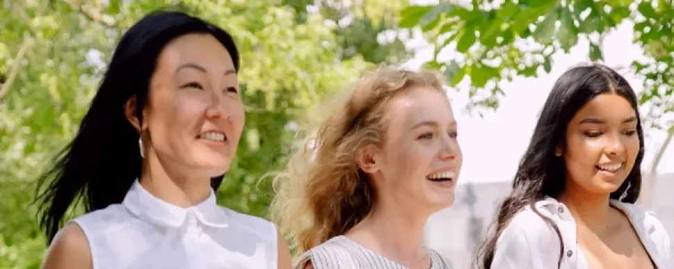 Three women walking outdoors, smiling and enjoying a sunny day.