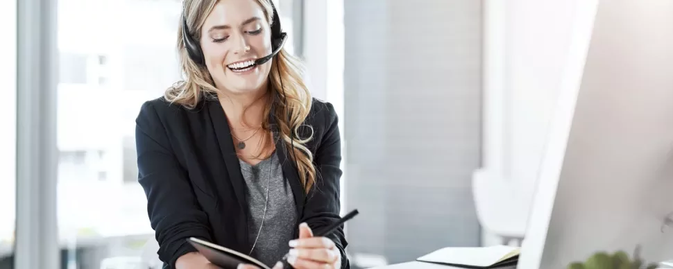 A woman wearing a headset holds a notepad, engaged in a discussion or taking notes.