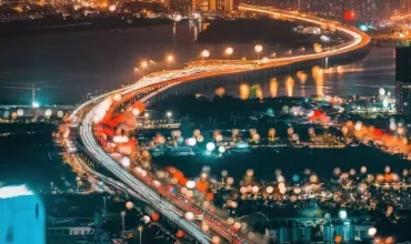 Aerial view of a city at night with a brightly lit bridge and blurred lights in the foreground.