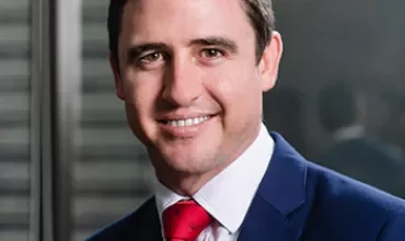 Man in a suit and red tie smiling indoors.