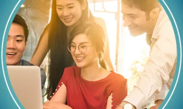 Group of four people happily looking at a laptop in a bright office.