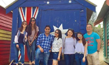 Group of people posing in front of a blue beach hut with an Australian flag design.