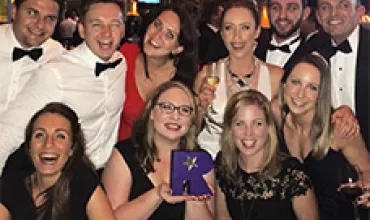 Group of people in formal attire at an event, some holding drinks and a purple award.