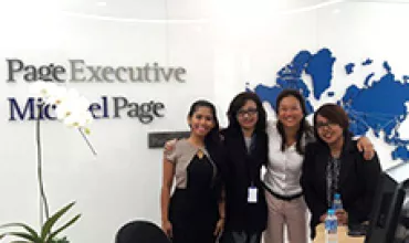 Four colleagues smiling in front of company logo and world map.