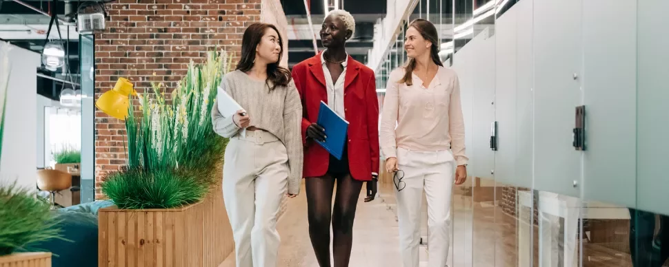 Three professionals walking in a modern office corridor with brick and glass walls.
