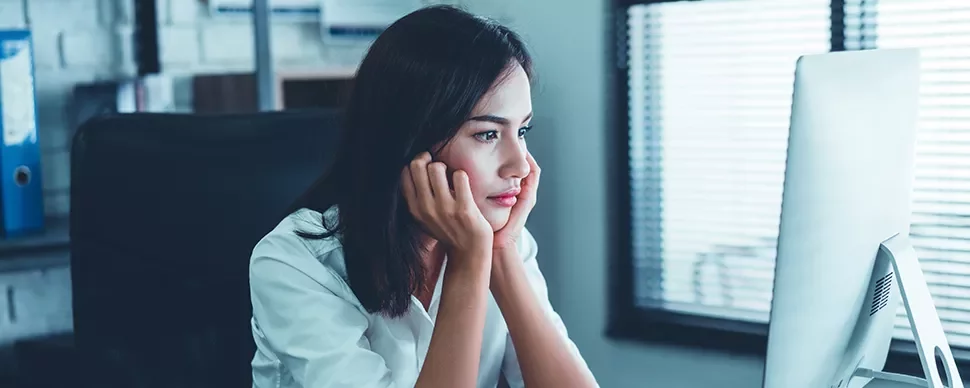 A woman in a white shirt staring intently at a computer screen in an office setting.