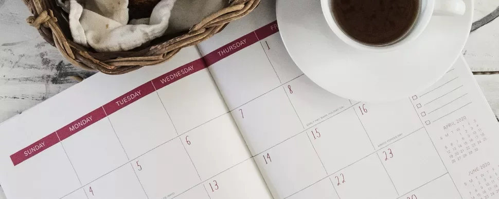 Open calendar with a basket and coffee cup on a white table.