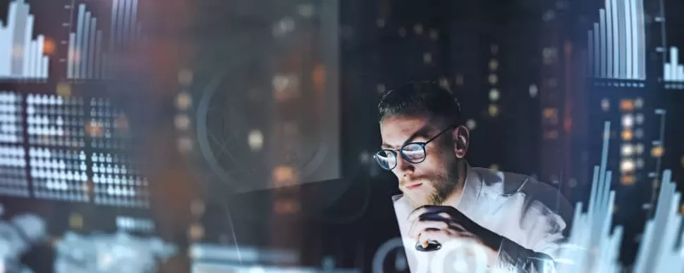 Man in glasses analyzes data on computer with blurred charts.