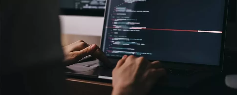 Person typing code on a laptop with a dark screen.