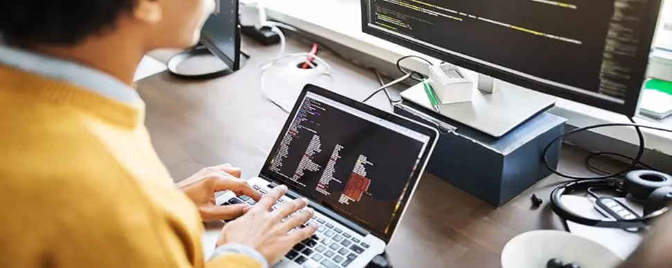 Person typing code on a laptop with a larger screen showing more code.