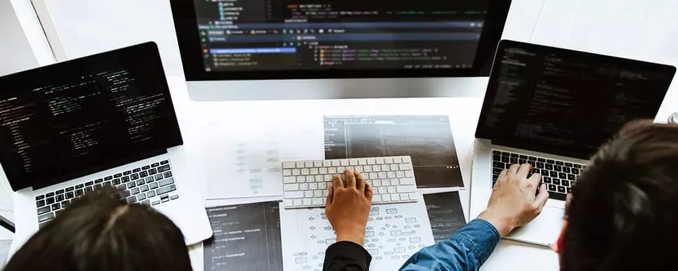 Three people working on laptops with code on screens.