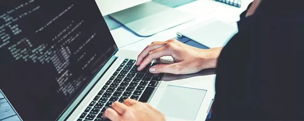 Person coding on a laptop with screen displaying lines of code.