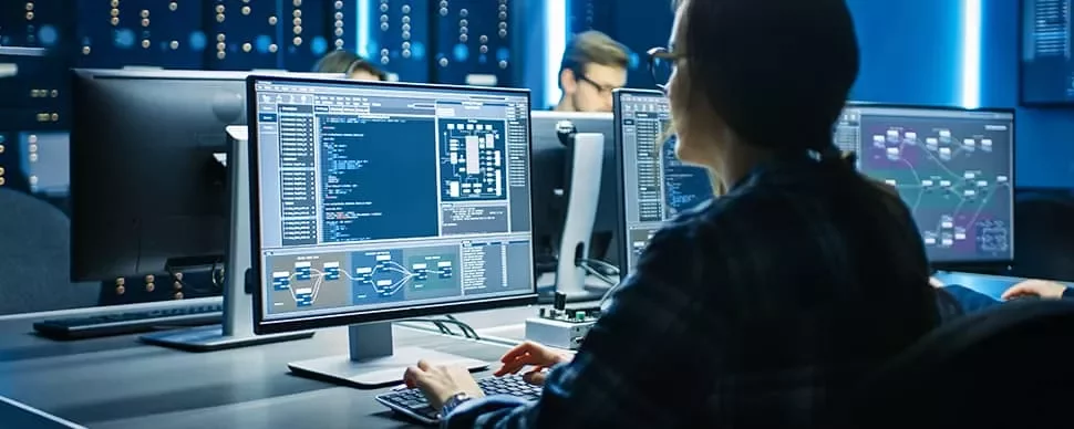 Person coding on computer in a dark room with screens